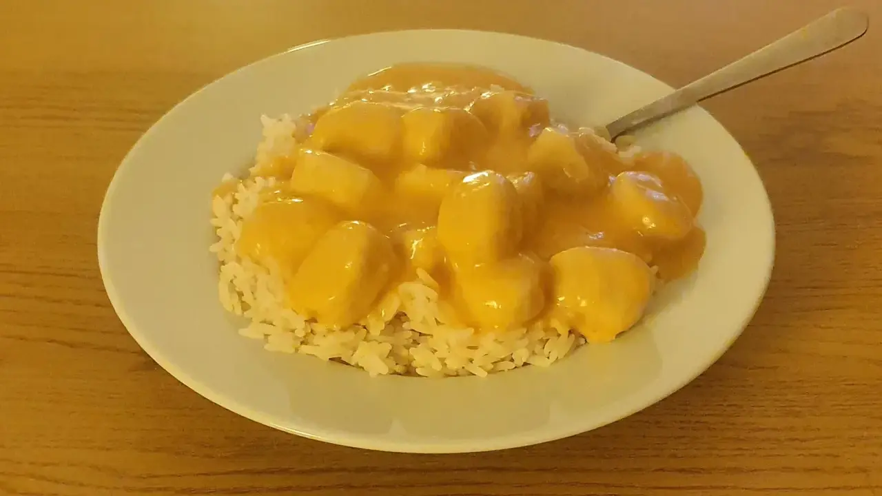 En tallrik med ris och krämiga fiskbullar i en gul sås. En nyttig och god måltid.