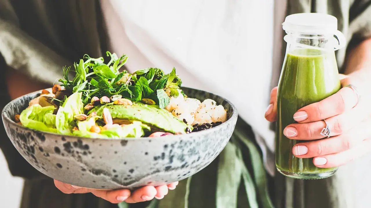 En person håller en skål med en hälsosam sallad och en grön smoothie. Perfekt mat att undvika gravid, med färska grönsaker och nötter.