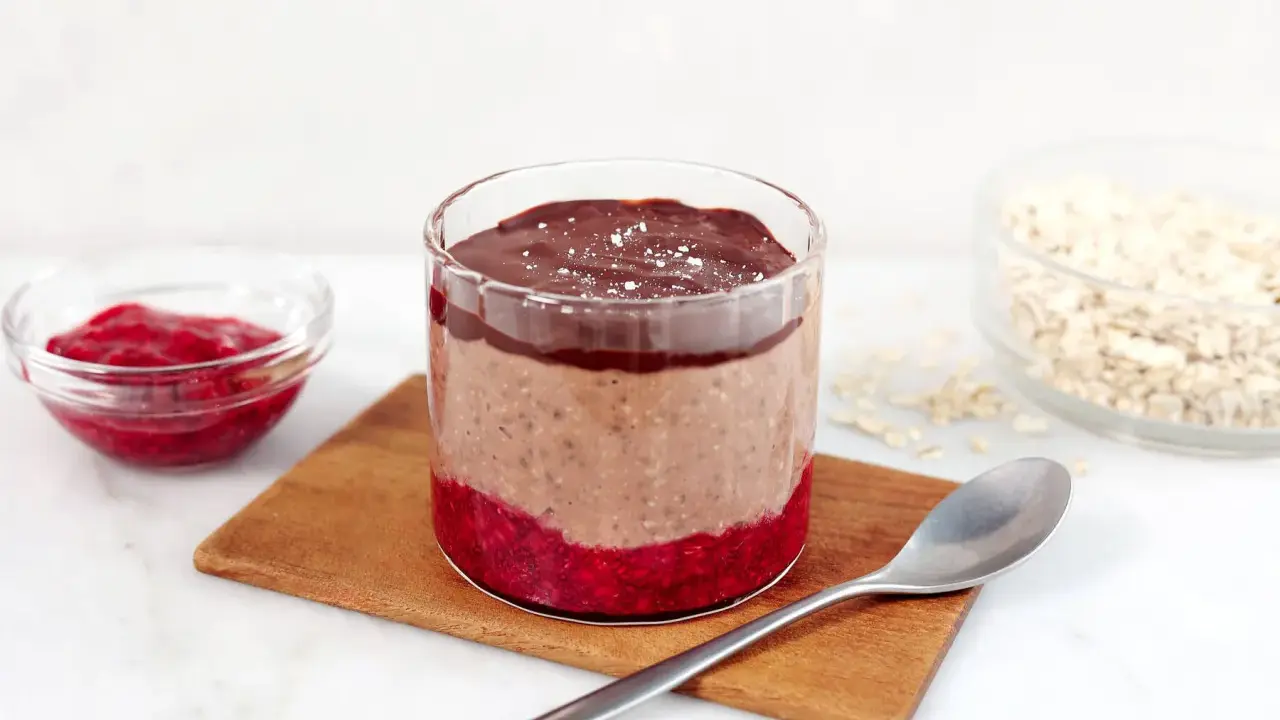 En glasburk med overnight oats propud choklad, hallonsylt och en sked.
