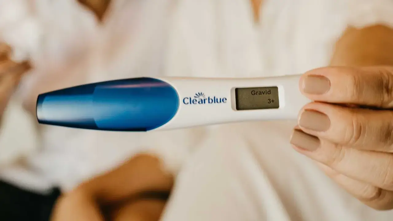 En hand håller ett digitalt graviditetstest som visar "Gravid 3+". En oväntad upptäckt, gravid utan att veta.