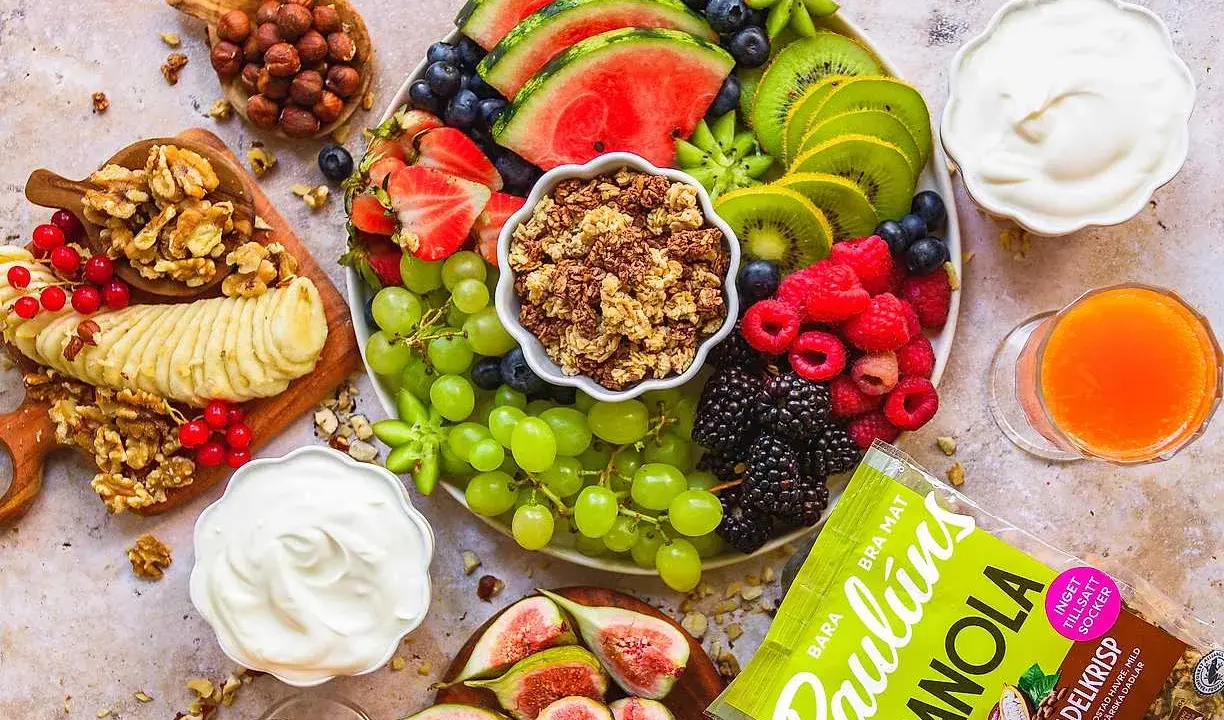 En lyxig frukostbricka med frukt, nötter, yoghurt och granola. Vattenmelon, kiwi, bär, vindruvor, banan och fikon skapar en färgsprakande och hälsosam start på dagen.