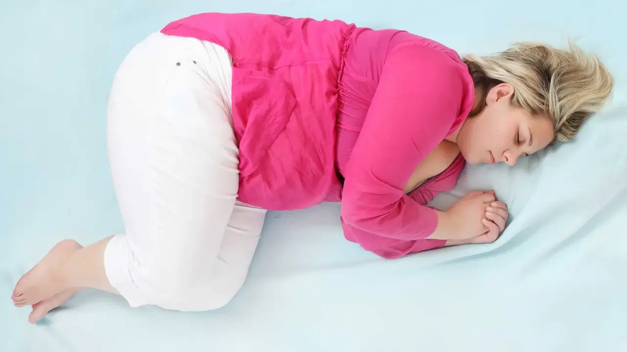 En kvinna i rosa tröja och vita byxor sover i fosterställning. V 34.