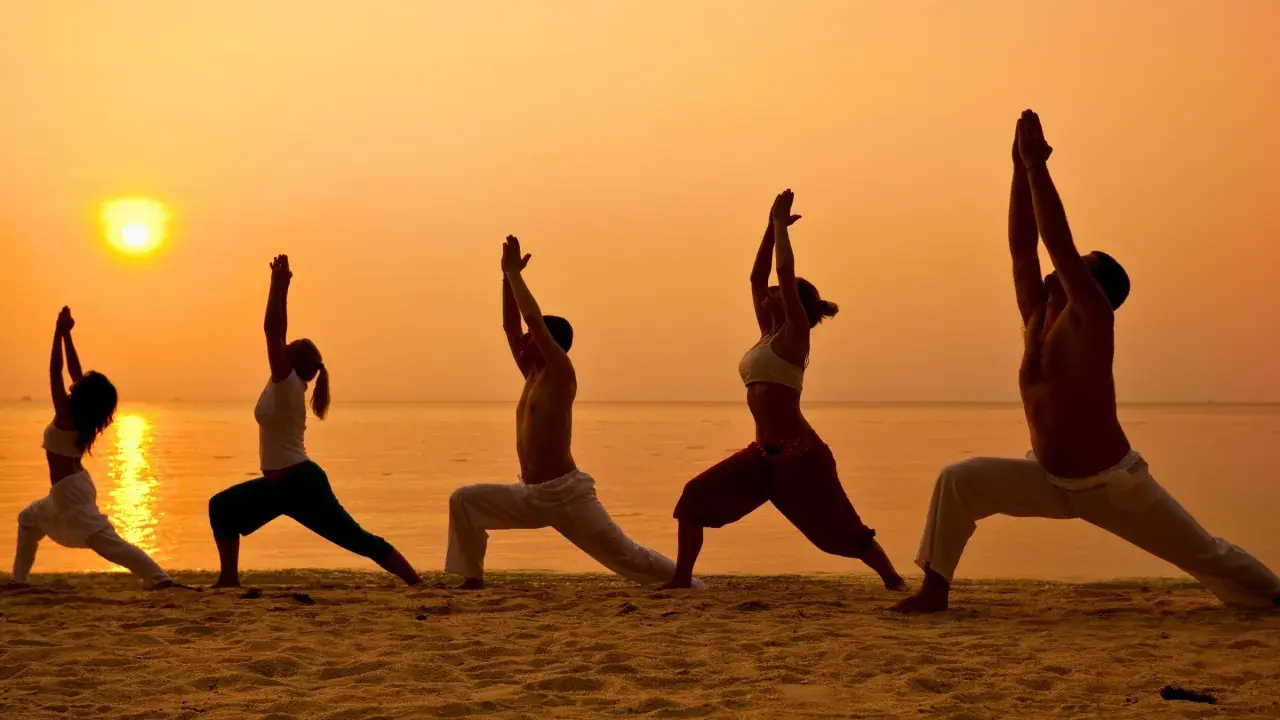 Silhuetter av människor som utövar yoga på en strand vid solnedgången. En fridfull yoga retreat Sverige upplevelse.