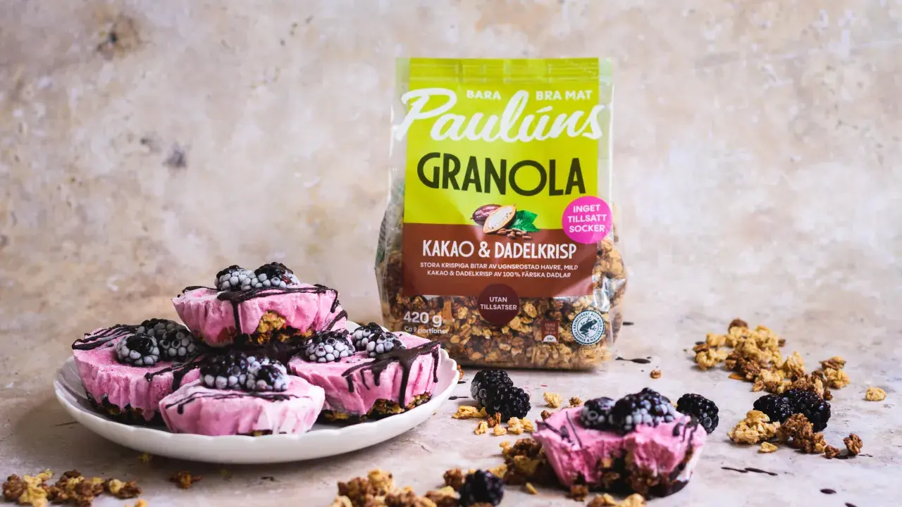 Rosa yoghurtglass med bär och granola, perfekt för ett snabbt yoghurtglass recept. Paulúns granola i bakgrunden.