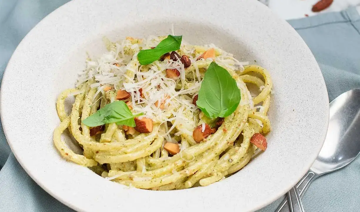 En portion krämig pasta med pesto, toppad med riven ost, nötter och basilika. Perfekt spagetti koktid för en snabb och god måltid.