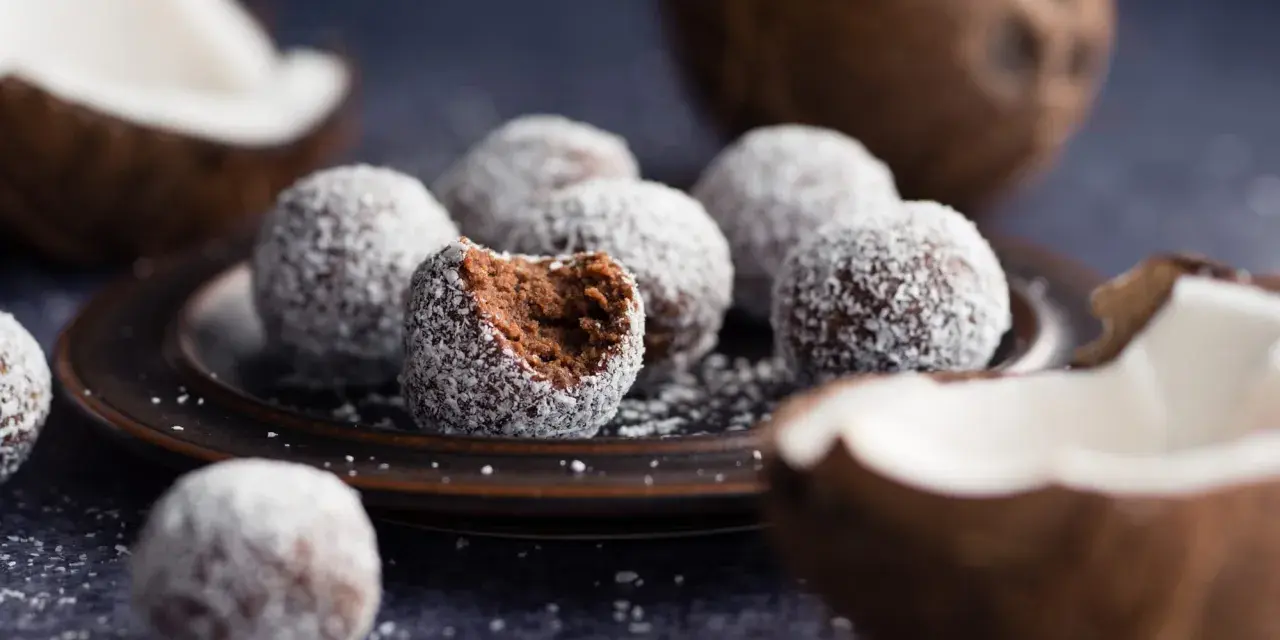 Chokladbollar med proteinpulver, rullade i kokos. En är uppäten, vilket avslöjar den mörka, saftiga insidan.