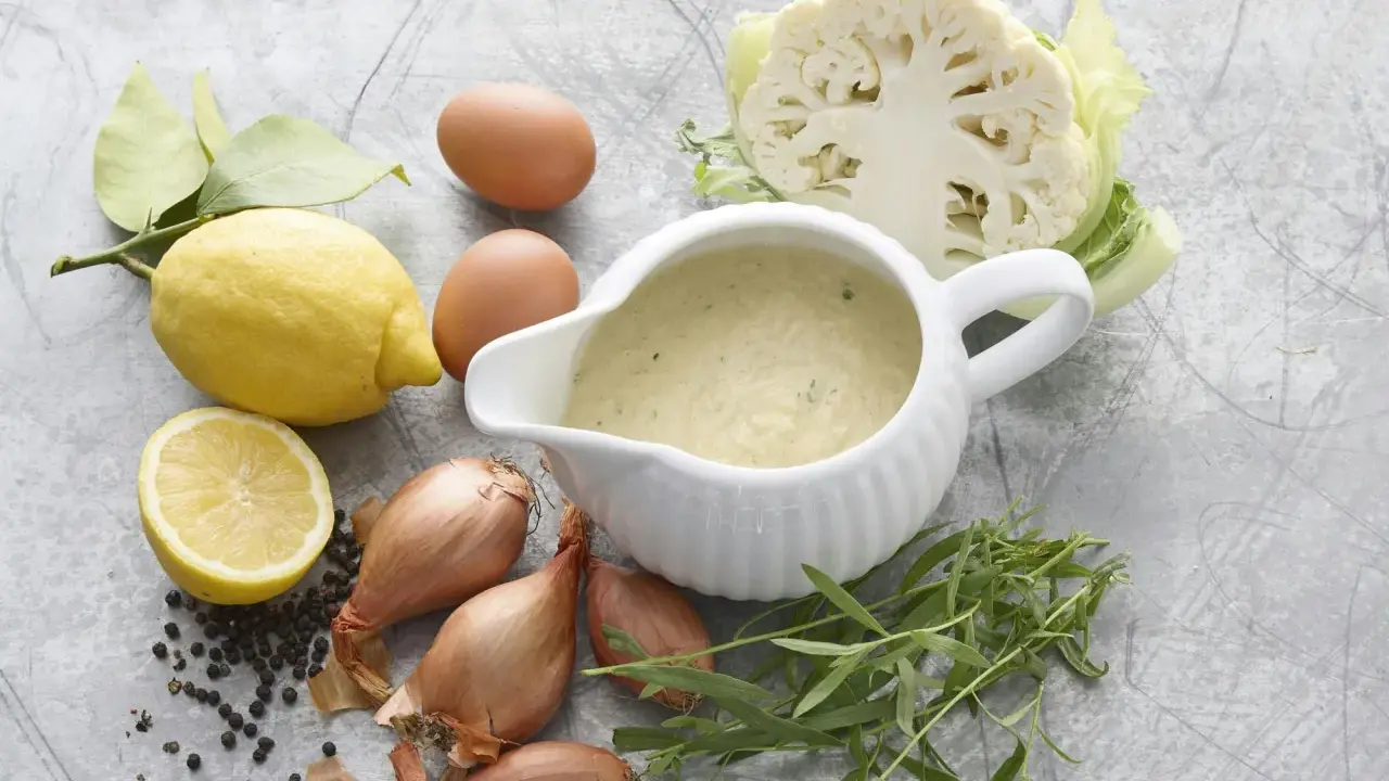En skål med nyttig bearnaisesås omgiven av ingredienser som citron, ägg, schalottenlök, pepparkorn, dragon och blomkål.