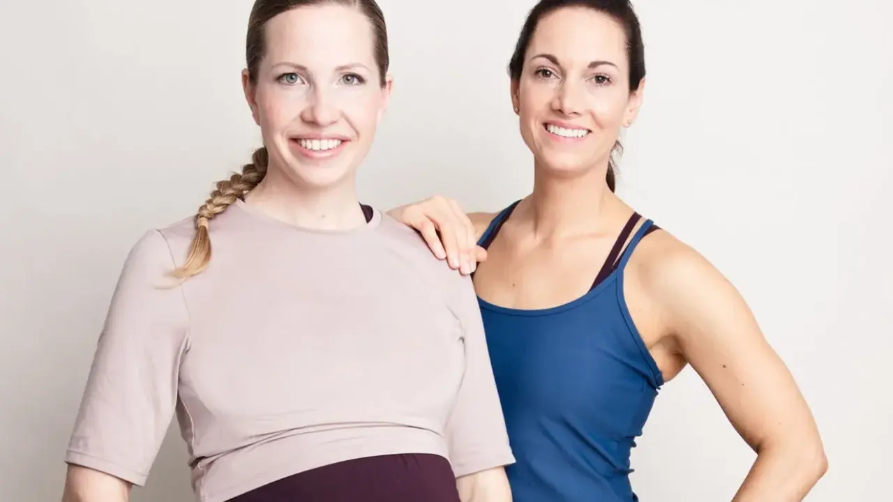 Två glada kvinnor, en gravid, poserar. De är klädda i träningskläder och ser ut att vara redo att lyfta tungt, gravid eller ej.