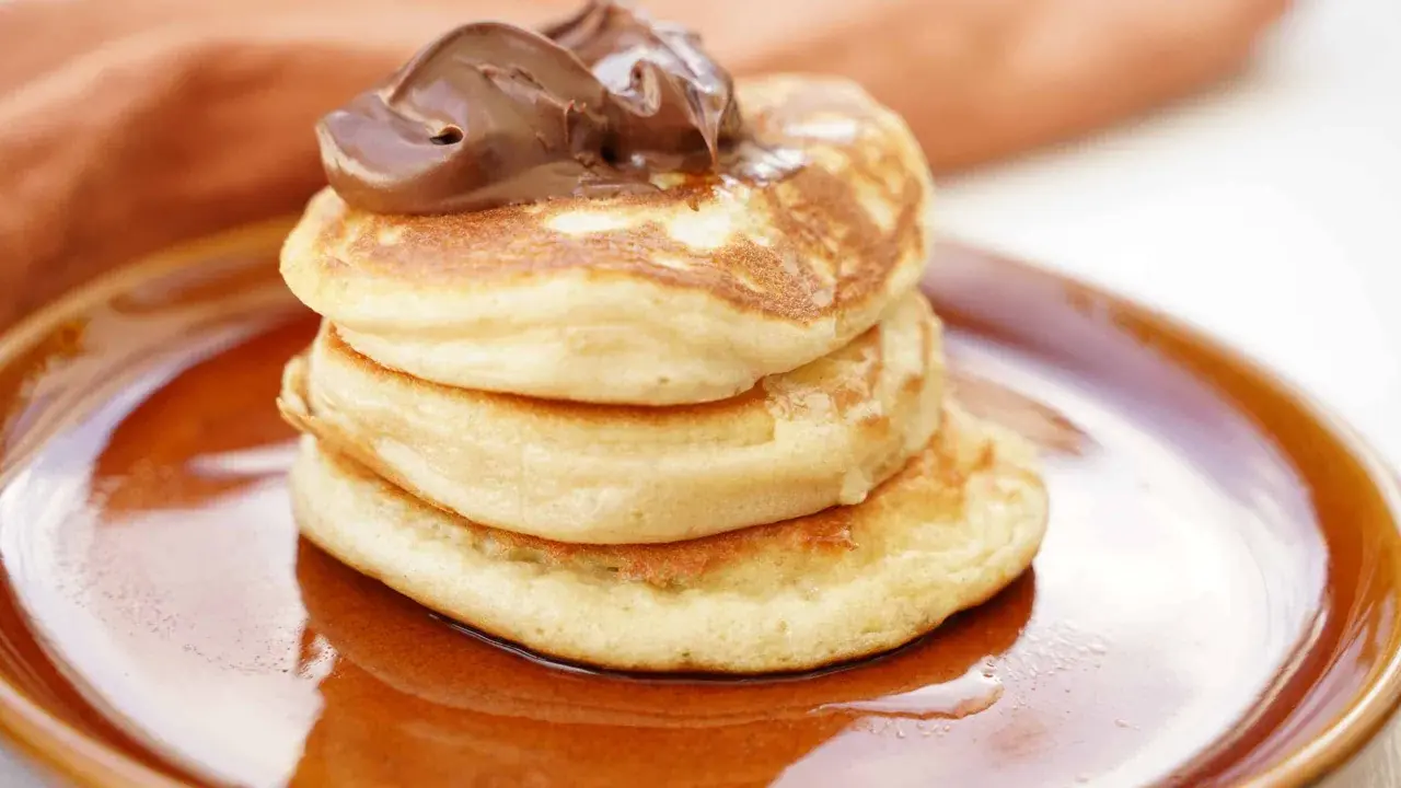 Amerikanska pannkakor med proteinpulver, toppade med chokladkräm, serveras på en brun tallrik. En hälsosam frukost!