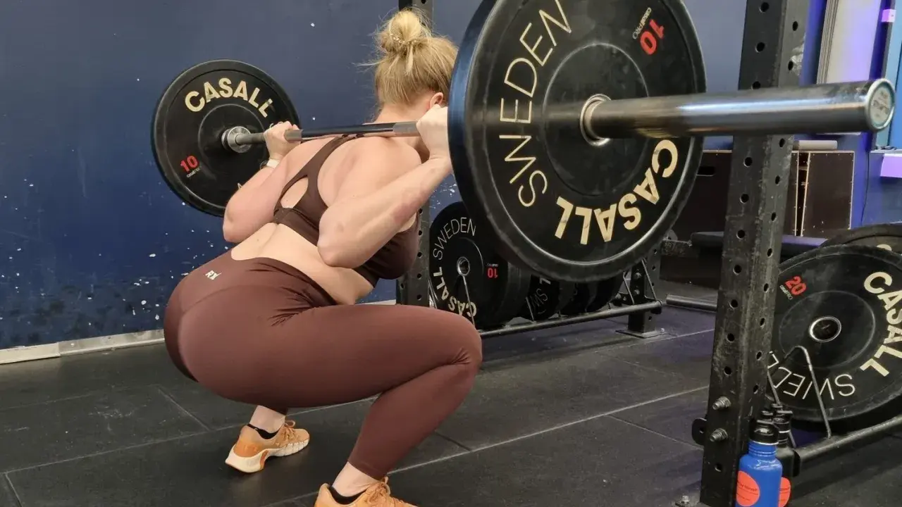 Kvinna utför en tung overhead squat med skivstång. Viktskivorna är märkta med "Casall Sweden".