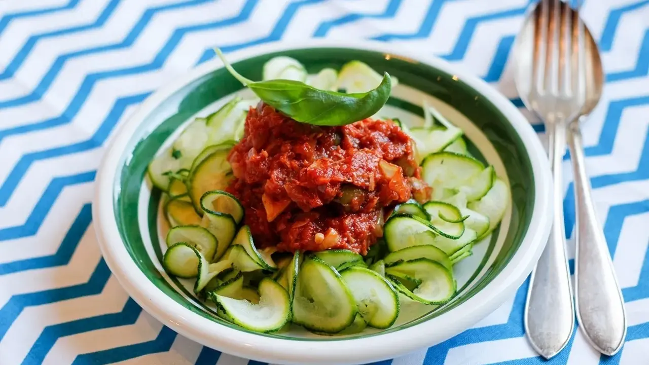 En skål med zucchinipasta och en smakrik tomatsås, toppad med basilika. Perfekt för goda nyttiga recept!