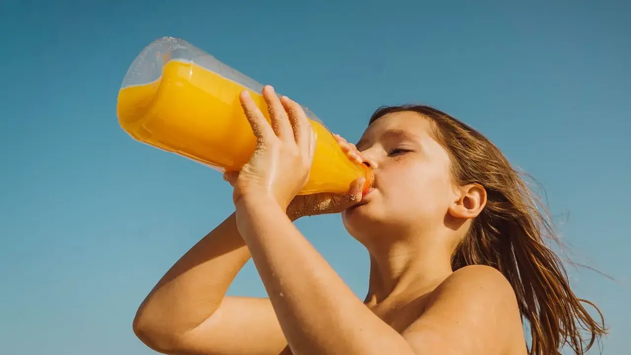 Barn dricker en stor flaska apelsinjuice, socker i juice ger energi på stranden.
