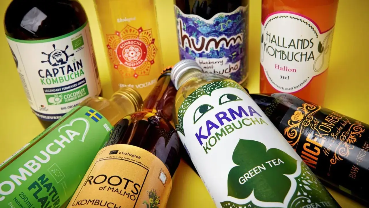Flera flaskor kombucha, en nyttig och fermenterad dryck, ligger utspridda. Olika märken som Captain Kombucha, Karma Kombucha och Hallands Kombucha syns.