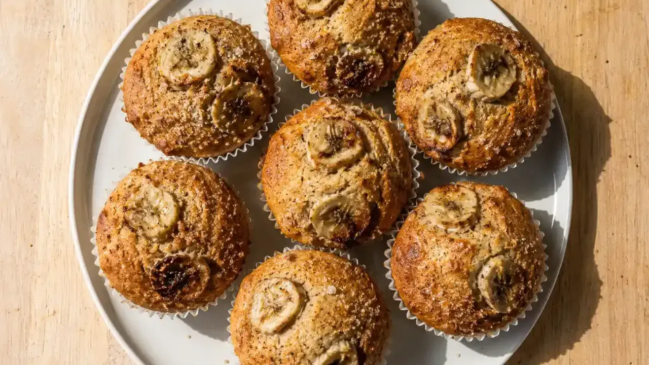 Sju gyllene bananmuffins med skivor av banan på toppen, redo att avnjutas. Ett perfekt bananmuffins recept för fika.