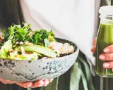 En person håller en skål med en hälsosam sallad och en grön smoothie. Perfekt mat att undvika gravid, med färska grönsaker och nötter.