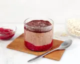 En glasburk med overnight oats propud choklad, hallonsylt och en sked.