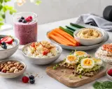 En hälsosam buffé med bärsmoothie, kvarg med frukt, nötter, äggmackor och grönsaker. Perfekt för ett proteinrikt mellanmål.