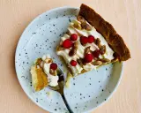 En bit glutenfri pumpapaj med vispgrädde, lingon och rostade pumpafrön på en prickig tallrik. En sked med en bit paj ligger bredvid.