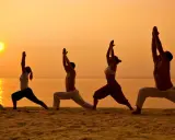 Silhuetter av människor som utövar yoga på en strand vid solnedgången. En fridfull yoga retreat Sverige upplevelse.