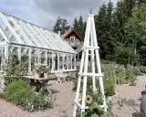 En vit rosentorn ritning står i en lummig trädgård med växthus och blommor.