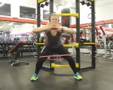 Kvinna utför krabbgång med gummiband runt benen i ett gym.
