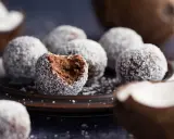 Chokladbollar med proteinpulver, rullade i kokos. En är uppäten, vilket avslöjar den mörka, saftiga insidan.