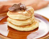 Amerikanska pannkakor med proteinpulver, toppade med chokladkräm, serveras på en brun tallrik. En hälsosam frukost!