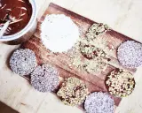 Riskakor med choklad och kokos eller pistage. En skål med smält choklad och en sked står bredvid.