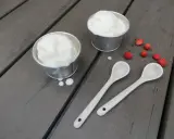 Två skålar med krämig glass på turkisk yoghurt, med vildhallon och skedar på en träyta.