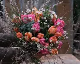 En bukett med rosa och orange tulpaner, omgiven av kvistar och små vita blommor. Vatten droppar från de gröna bladen.