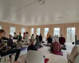 Människor sitter på kuddar och stolar under en meditation retreat i Sverige. En person i munkkläder leder sessionen.
