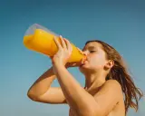 Barn dricker en stor flaska apelsinjuice, socker i juice ger energi på stranden.