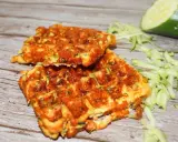Gyldene zucchini våfflor, perfekt stekta, med riven zucchini och en hel zucchini i bakgrunden.