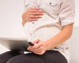 Gravid kvinna sitter på toaletten med en surfplatta, oroar sig för brun flytning.