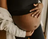 En gravid mage i tredje trimestern, varsamt omfamnad av händer. En ljus skjorta draperad över axeln.
