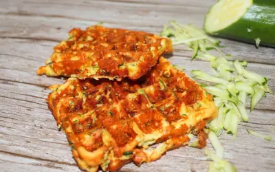 Gyldene zucchini våfflor, perfekt stekta, med riven zucchini och en hel zucchini i bakgrunden.