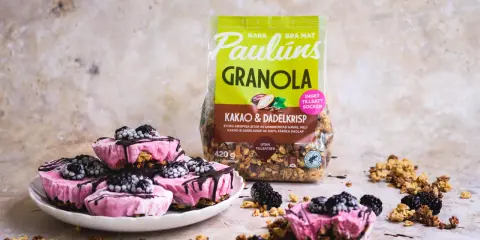 Rosa yoghurtglass med bär och granola, perfekt för ett snabbt yoghurtglass recept. Paulúns granola i bakgrunden.