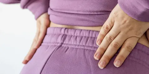 Händer vilar på ryggslut och höfter, en påminnelse om hormonell obalans efter graviditet.