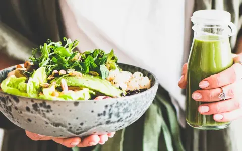 En person håller en skål med en hälsosam sallad och en grön smoothie. Perfekt mat att undvika gravid, med färska grönsaker och nötter.