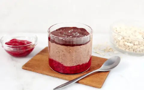 En glasburk med overnight oats propud choklad, hallonsylt och en sked.