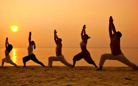Silhuetter av människor som utövar yoga på en strand vid solnedgången. En fridfull yoga retreat Sverige upplevelse.