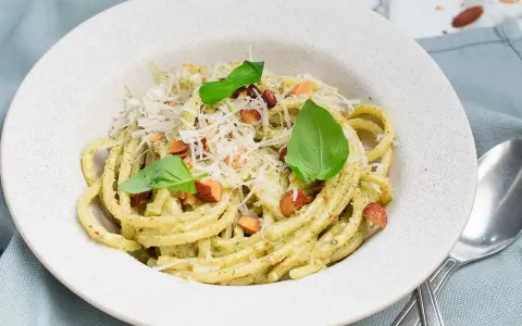 En portion krämig pasta med pesto, toppad med riven ost, nötter och basilika. Perfekt spagetti koktid för en snabb och god måltid.