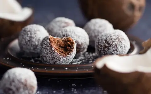 Chokladbollar med proteinpulver, rullade i kokos. En är uppäten, vilket avslöjar den mörka, saftiga insidan.