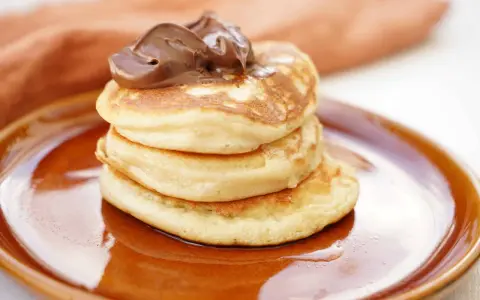 Amerikanska pannkakor med proteinpulver, toppade med chokladkräm, serveras på en brun tallrik. En hälsosam frukost!
