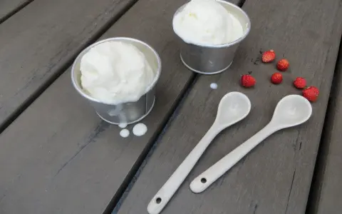 Två skålar med krämig glass på turkisk yoghurt, med vildhallon och skedar på en träyta.