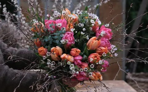 En bukett med rosa och orange tulpaner, omgiven av kvistar och små vita blommor. Vatten droppar från de gröna bladen.