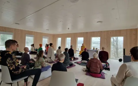 Människor sitter på kuddar och stolar under en meditation retreat i Sverige. En person i munkkläder leder sessionen.