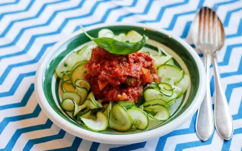 En skål med zucchinipasta och en smakrik tomatsås, toppad med basilika. Perfekt för goda nyttiga recept!