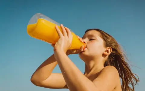 Barn dricker en stor flaska apelsinjuice, socker i juice ger energi på stranden.