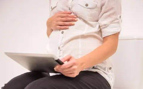 Gravid kvinna sitter på toaletten med en surfplatta, oroar sig för brun flytning.